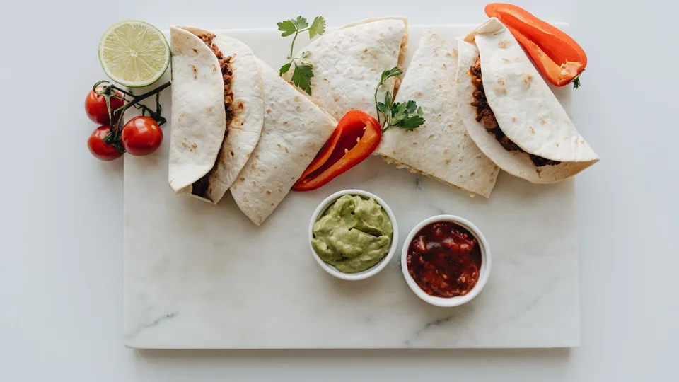 Tacos servidos en una tabla con guacamole y salsa